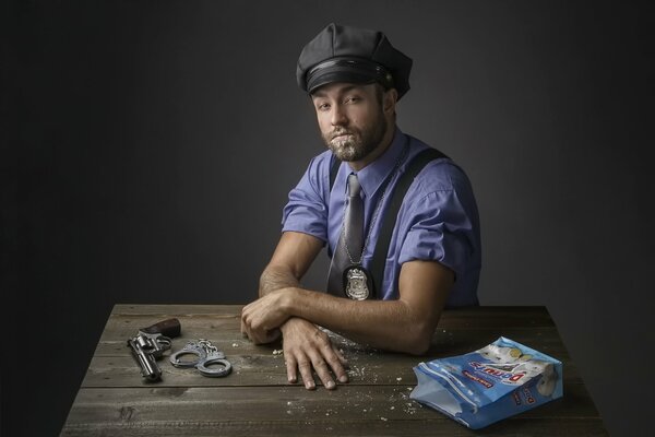 Коп позирует для фотоснимка. На столе револьвер, наручники и пакет с пончиками